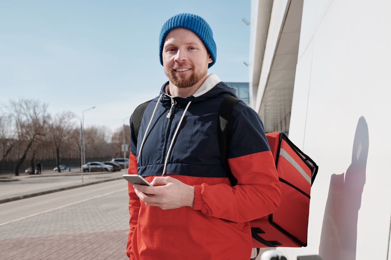 Man in casual wear holding phone, ready for delivery on sunny day.