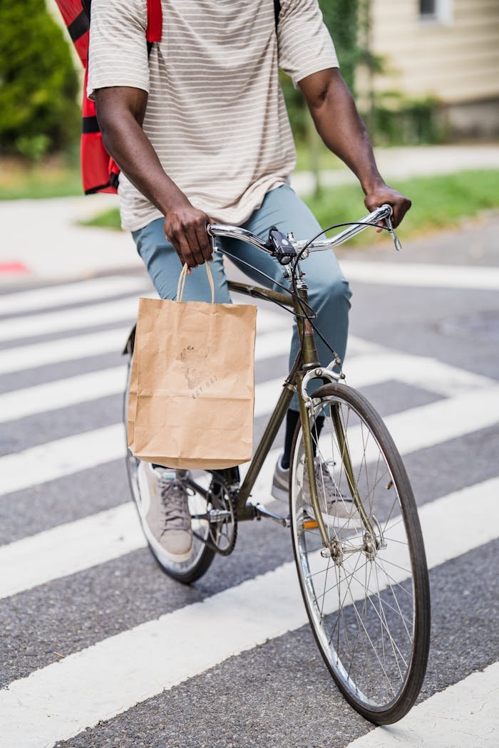 Bicycle courier delivering a package while crossing a street in an urban area.