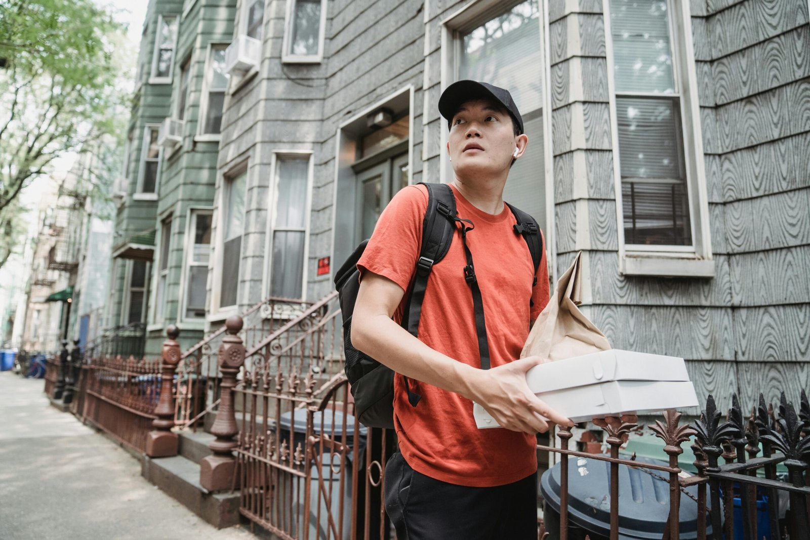 pexels photo 9461606 9461606 A delivery worker in a red shirt and cap holding packages outside a residential building.